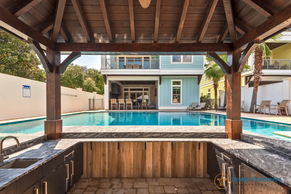 The photo features a sparkling swimming pool, an outdoor kitchen, and a covered patio, all set in a luxurious and relaxed environment. The setup welcomes guests to gather for sunset dinners or poolside celebrations, highlighting the flexible entertainment and dining options available.