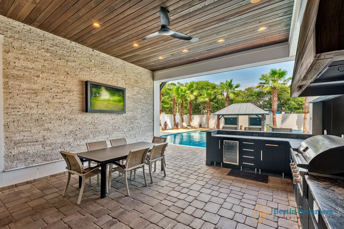 An inviting outdoor area featuring a swimming pool, outdoor kitchen, dining table, and palm trees. The space is set up for outdoor dining, barbecues, pool parties, and relaxation, capturing the essence of a private resort experience.