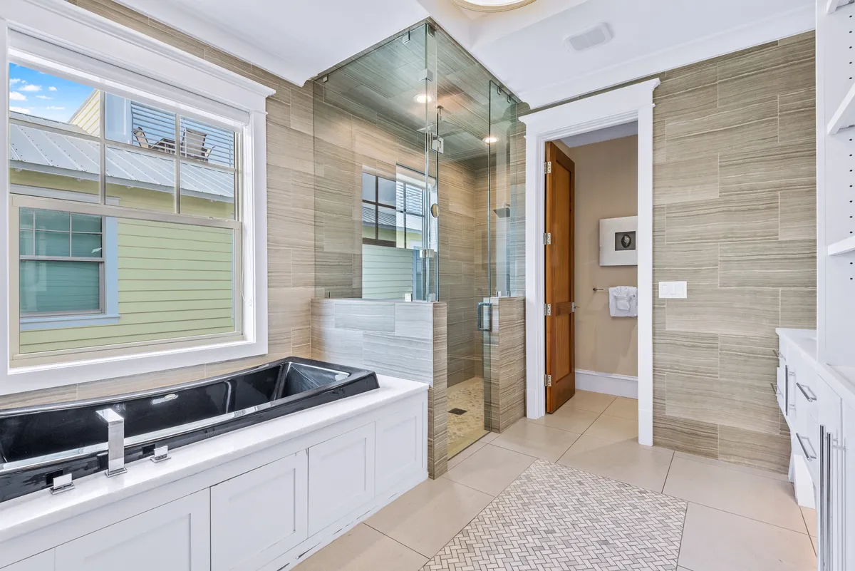 A serene, spa-inspired bathroom featuring a freestanding black bathtub, a walk-in shower, double vanity, and a large window letting in natural light. The space exudes tranquility and luxury, perfect for unwinding after a full day.