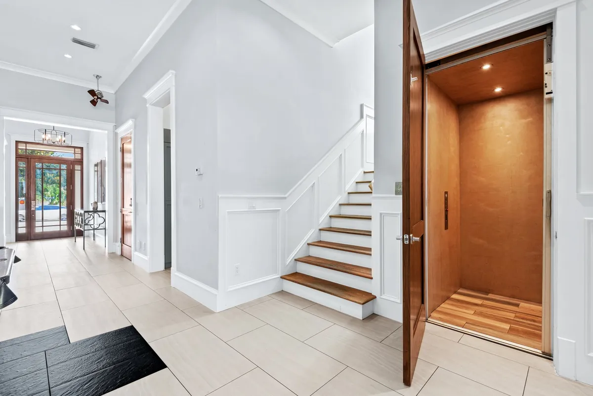 A modern, inviting foyer featuring a staircase and an elevator, with the front door nearby. The elevator is clearly visible, emphasizing accessibility for all guests and the ease of moving between floors.