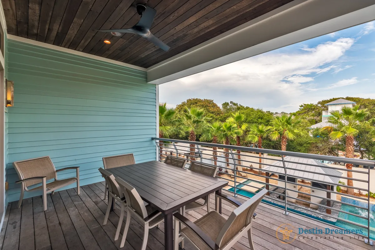An outdoor balcony dining area with a table surrounded by palm trees and a sturdy railing, offering views and an inviting ambiance for al fresco dining, sunset dinners, or after-dinner relaxation overlooking the pool.