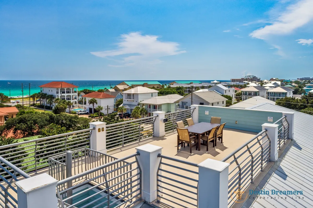 A spacious rooftop patio with a dining table and chairs, modern metal railing, and sweeping views of the ocean and colorful rooftops. The setting is perfect for sunset cocktails, al fresco meals, or stargazing with friends after a day of adventure.