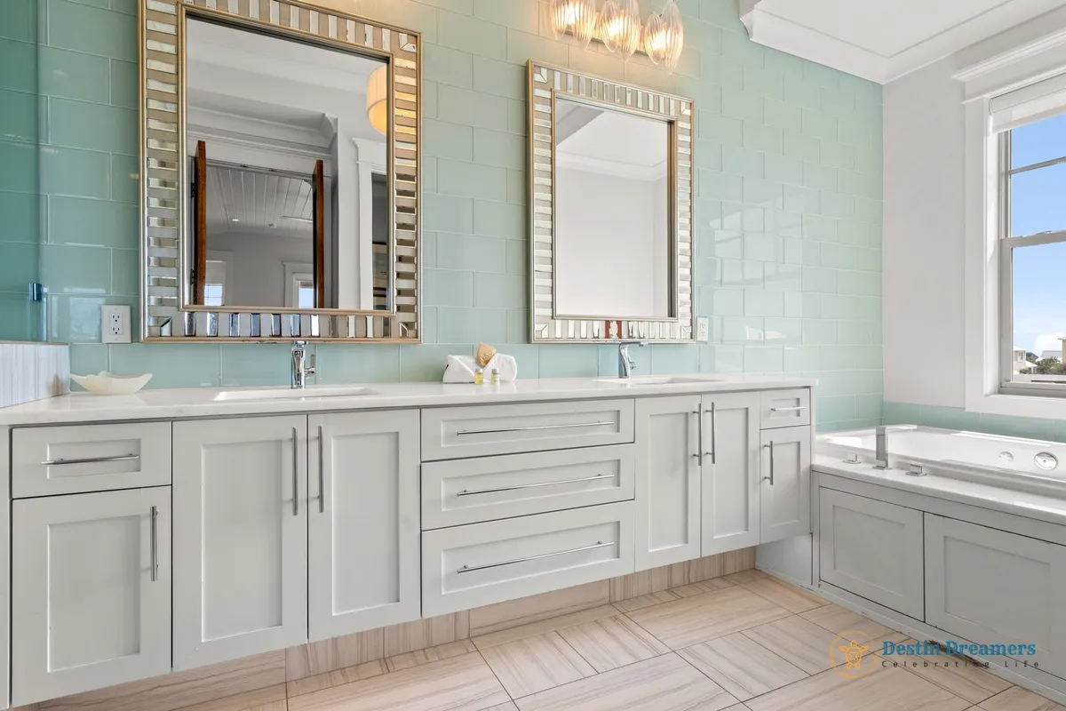 A bright, spa-inspired bathroom with dual sinks, modern cabinetry, and two large decorative mirrors. A luxurious jacuzzi tub sits by the window, surrounded by light aqua tiles, offering a rejuvenating space for relaxation after a day of adventures.