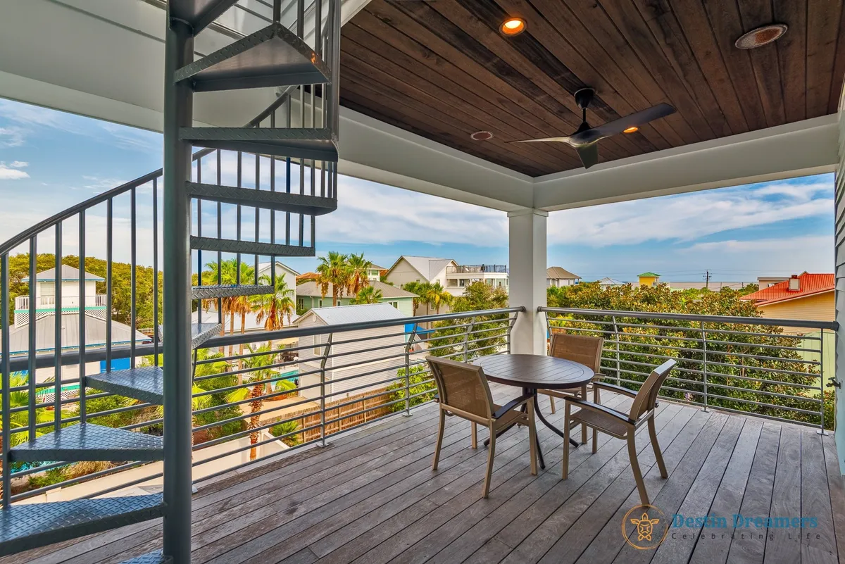 An inviting spiral staircase leads up to a rooftop patio with covered outdoor seating. The balcony offers wide views of the surrounding neighborhood and glimpses of the distant Gulf, ideal for sunrise or sunset relaxation.