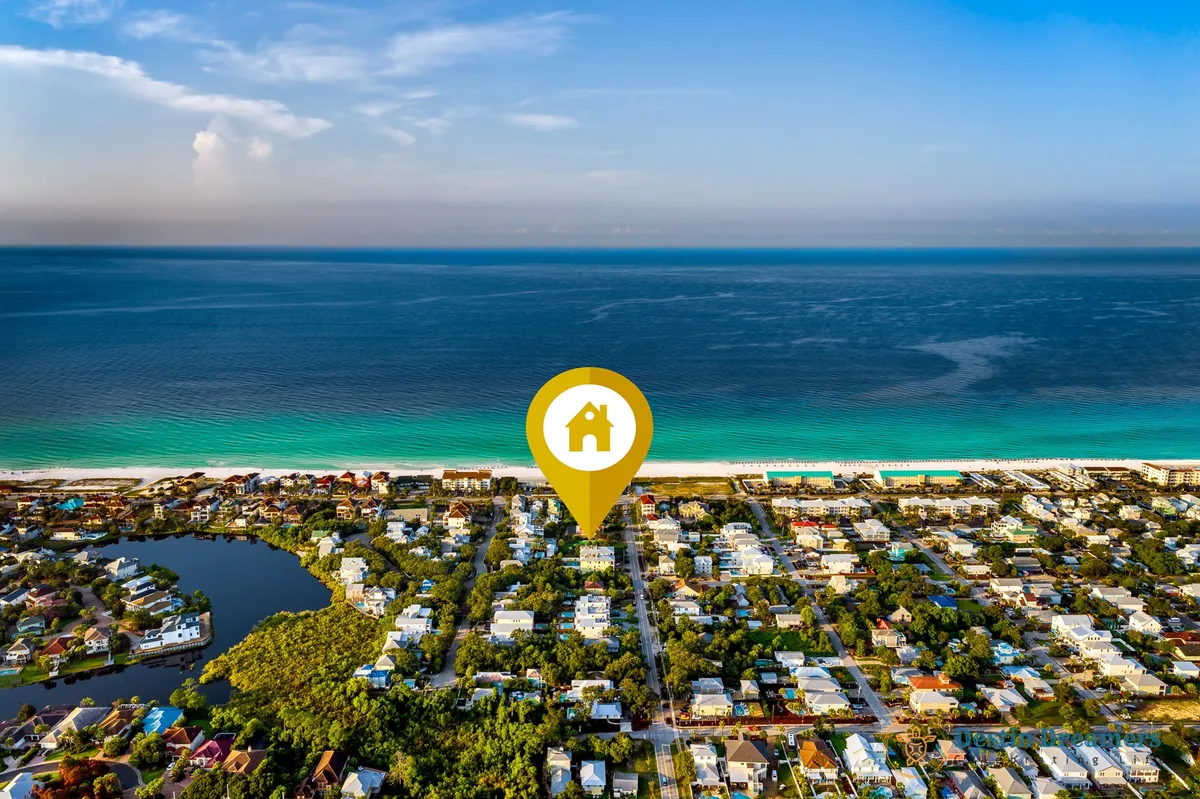 A panoramic aerial view marking The Life Aquatic property with a yellow icon, set amidst a picturesque stretch of sugar-white beach and turquoise Gulf waters, surrounded by a lush residential neighborhood. The expansive coastline and blue sky underscore the proximity to natural and local attractions.