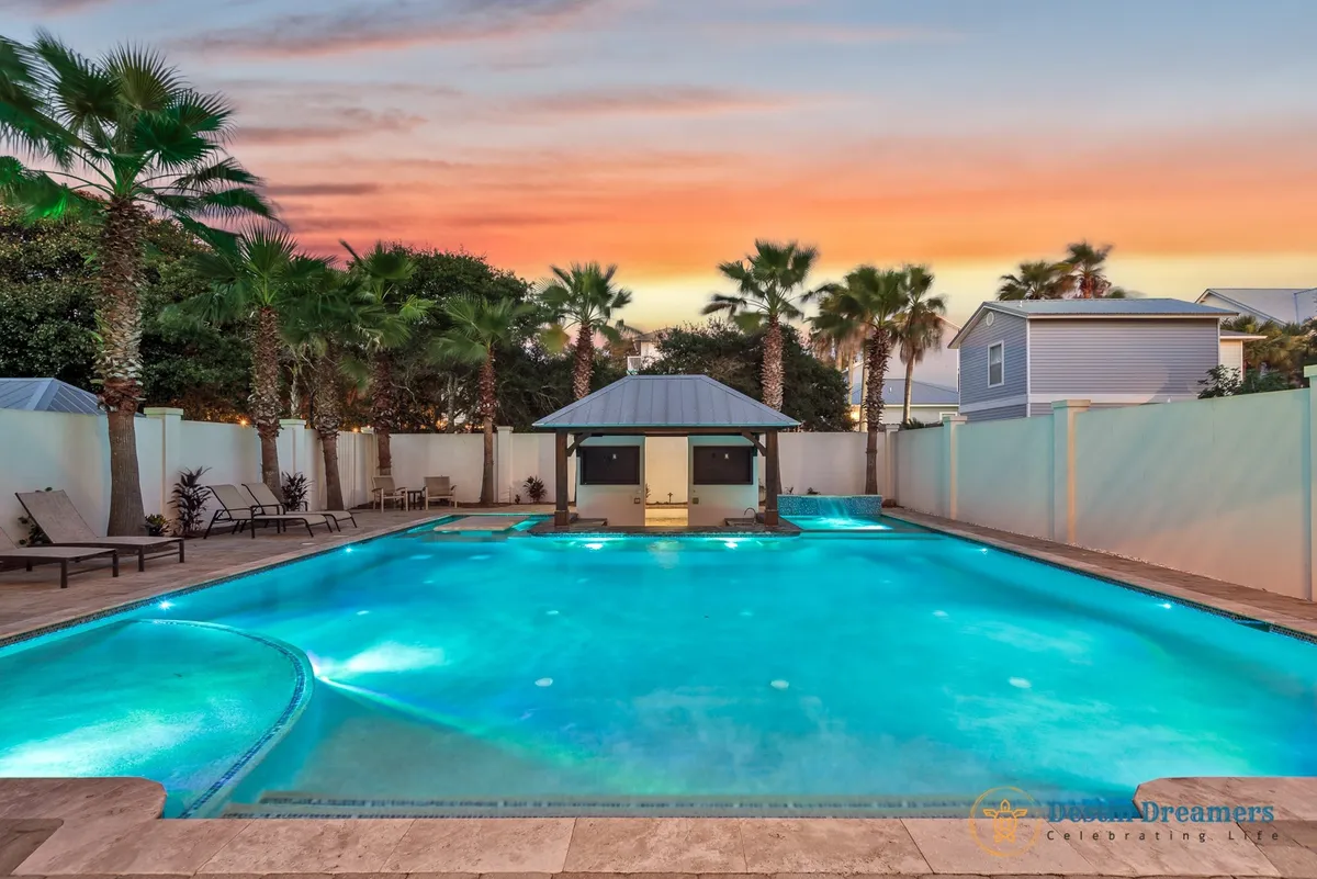 A private heated pool with a sunken swim-up bar and poolside hot tub, all surrounded by a tiki-style kitchen/bar area, palm trees, and privacy walls. The setting exudes a relaxing, upscale vacation vibe, perfect for unwinding after a day of adventure.